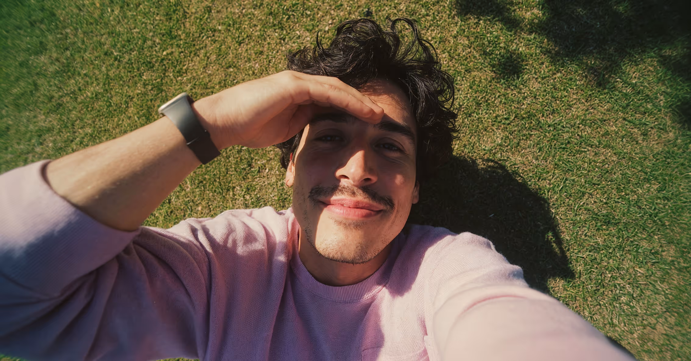 Criador deitado na grama, sorrindo, olhando para o celular
